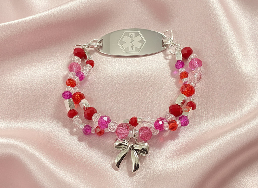Beaded bracelet with medical alert tag and bow charm on a black background