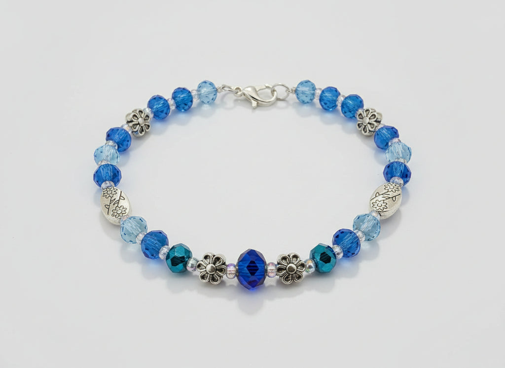 Blue beaded bracelet with floral and leaf designs on a dark background