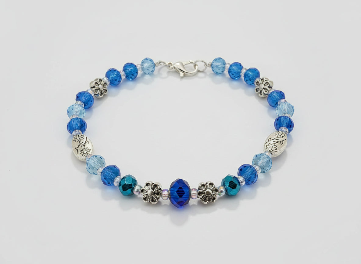 Blue beaded bracelet with floral and leaf designs on a dark background
