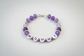 Bracelet with purple beads and letter beads spelling 'MOM' on a dark background