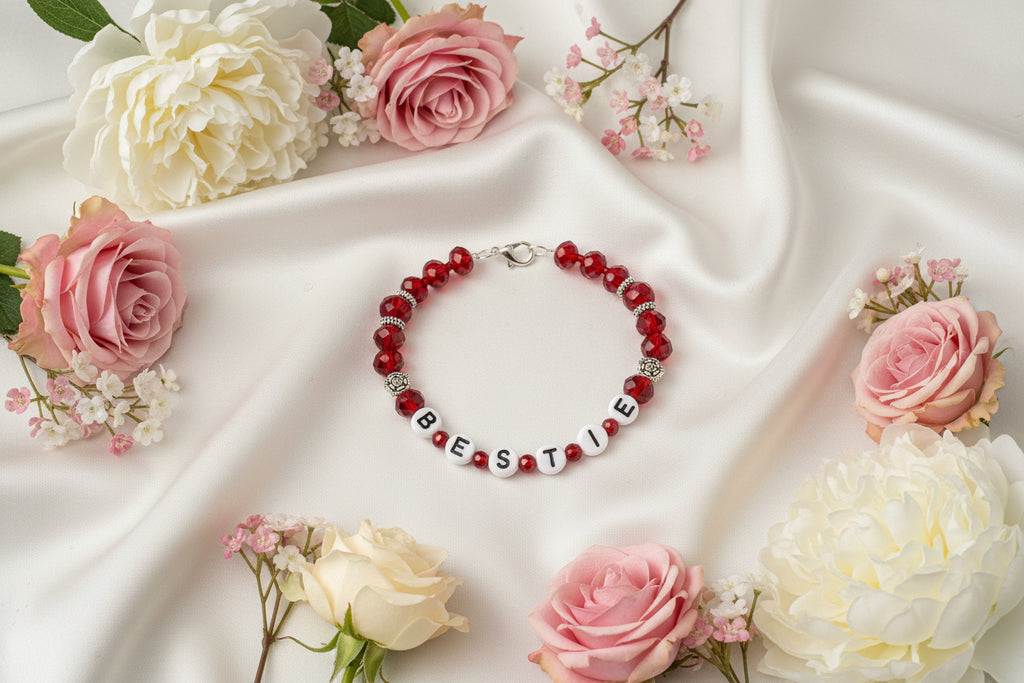 Bracelet with red beads and letter beads spelling 'BESTIE' on a dark background