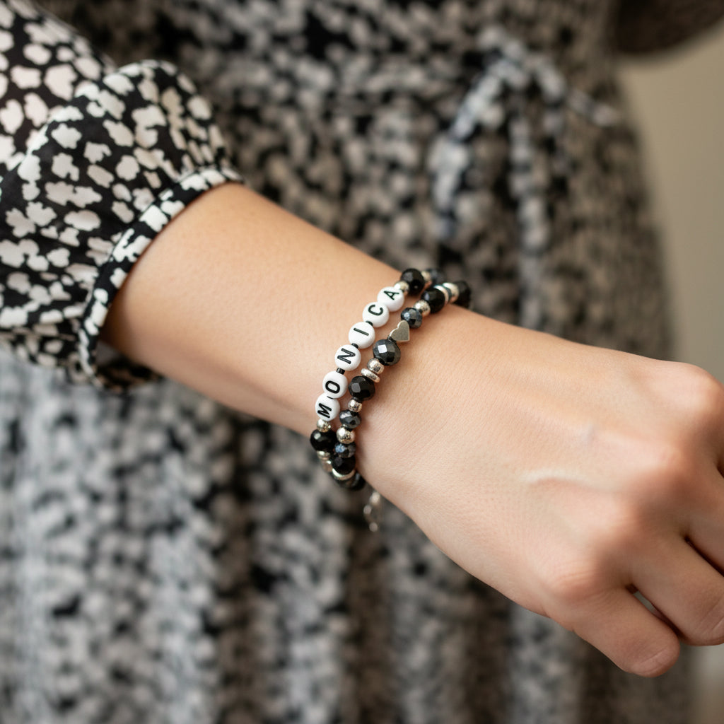 Bracelet with black beads and letter beads spelling 'MONICA' on a dark surface