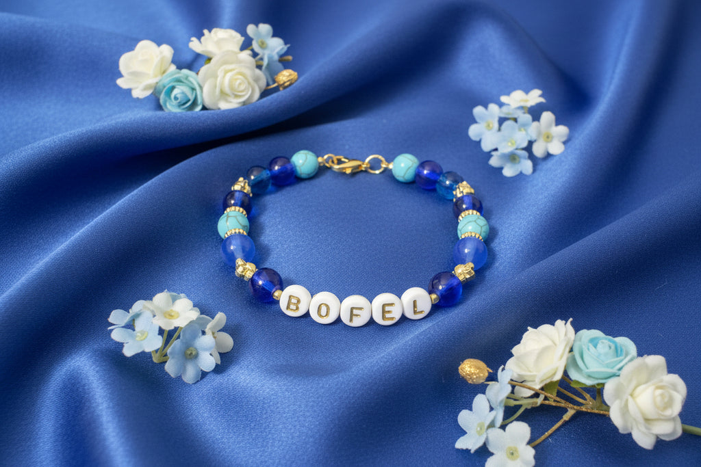 Bracelet with letter beads spelling 'BOFEL' on a dark fabric background