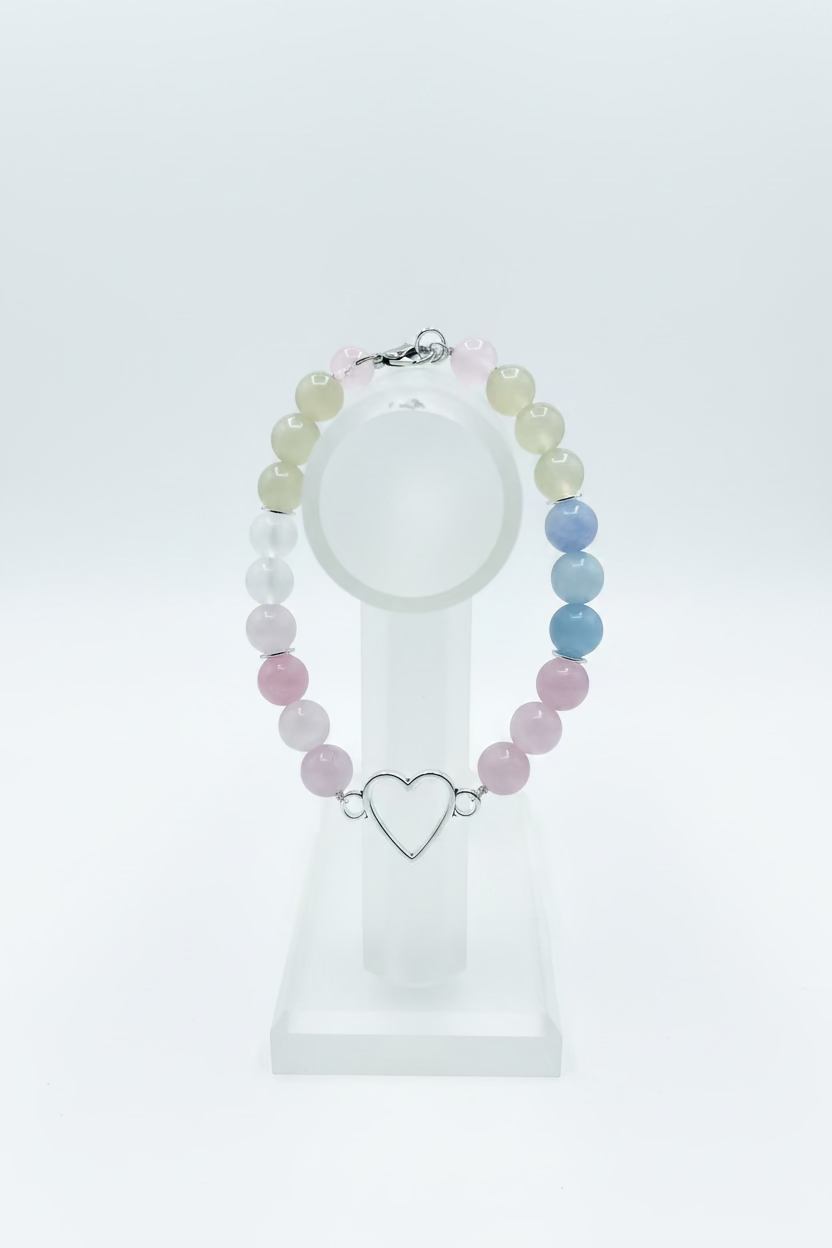 A beaded bracelet with pink, light green, and blue round beads, featuring a silver-tone open heart charm in the center, displayed on a light wood background.