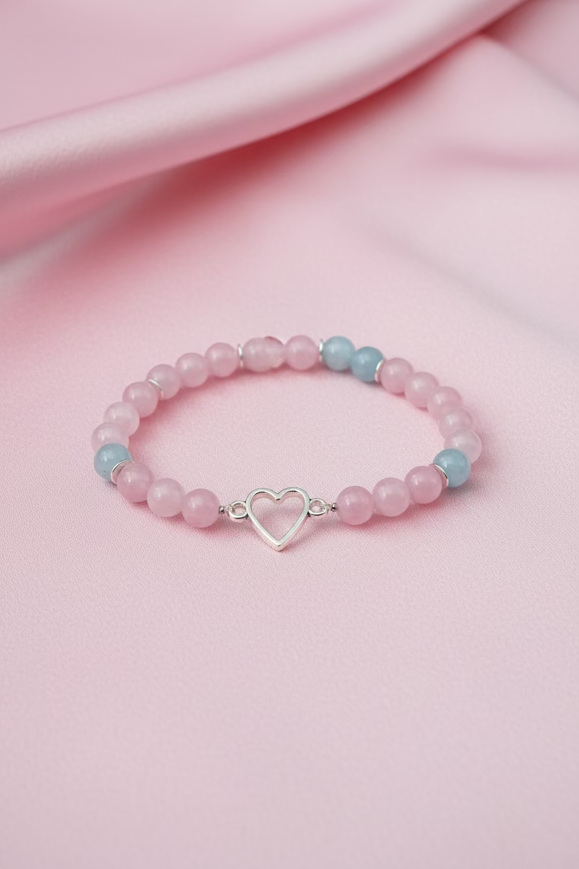 A beaded bracelet with light pink and light blue beads and a silver heart-shaped charm, displayed on a light wood hanger card over a wooden surface.