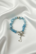 A beaded stretch bracelet made of light blue stone chips with a silver toggle clasp and dangling heart charm, displayed on a dark textured surface.