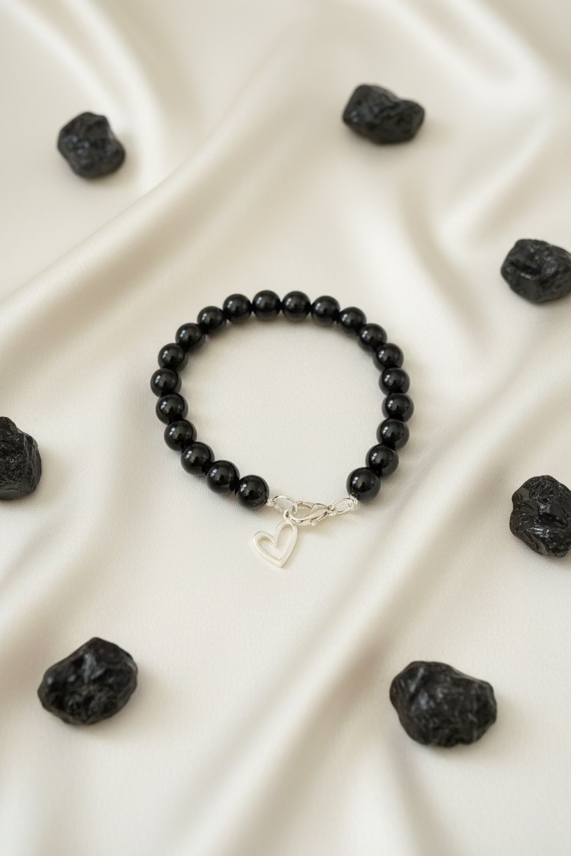 A black beaded bracelet with a silver lobster clasp and a dangling open heart charm, displayed on a dark textured surface.