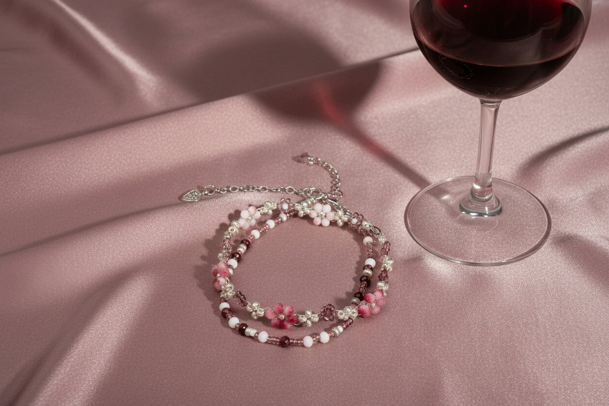 A beaded double-strand bracelet featuring pink flower beads, white pearl-like beads, and metallic gold and silver beads, displayed on a dark textured background.