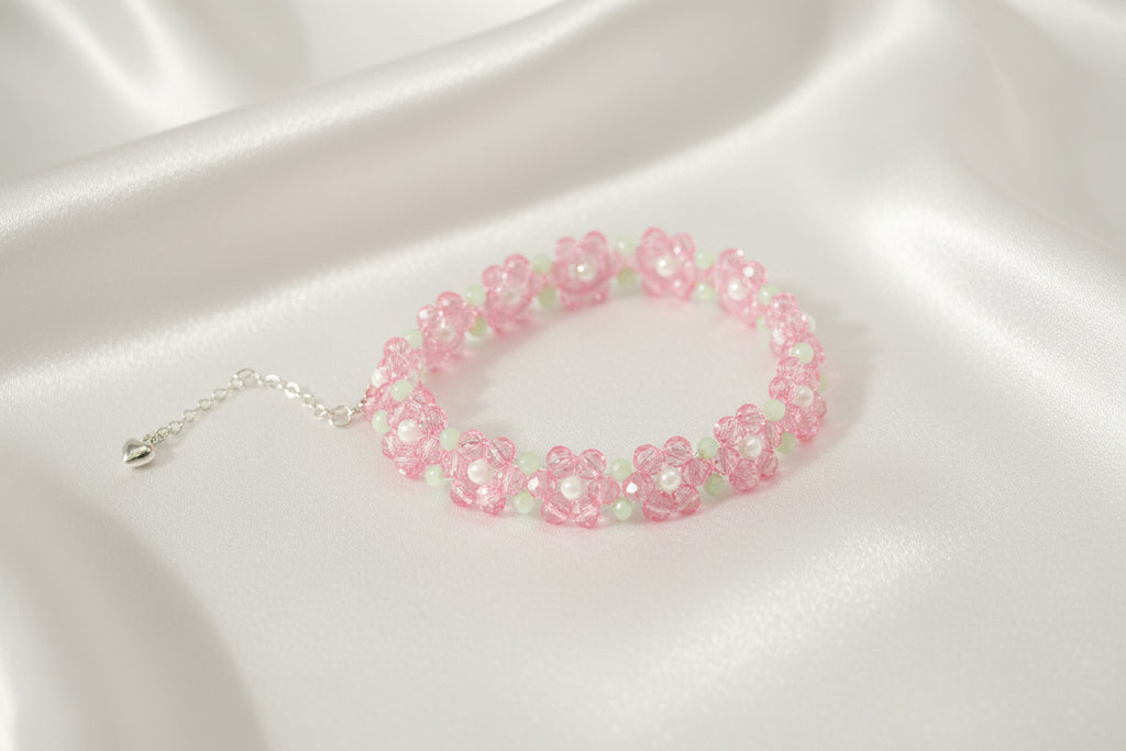 A beaded stretch bracelet featuring pink flower motifs with light green centers and silver-tone chain extender, displayed on a dark textured background.