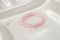 A beaded stretch bracelet featuring pink flower motifs with light green centers and silver-tone chain extender, displayed on a dark textured background.