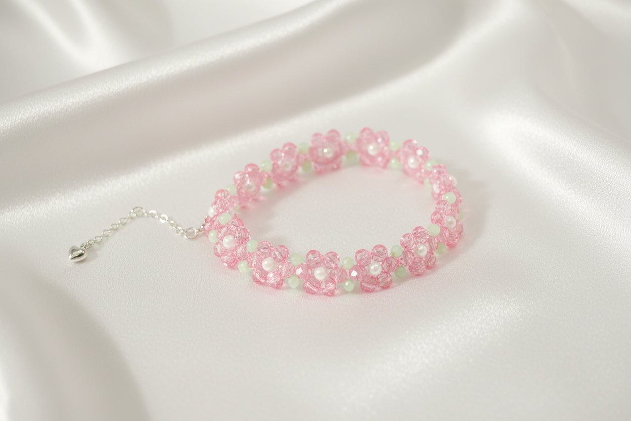 A beaded stretch bracelet featuring pink flower motifs with light green centers and silver-tone chain extender, displayed on a dark textured background.