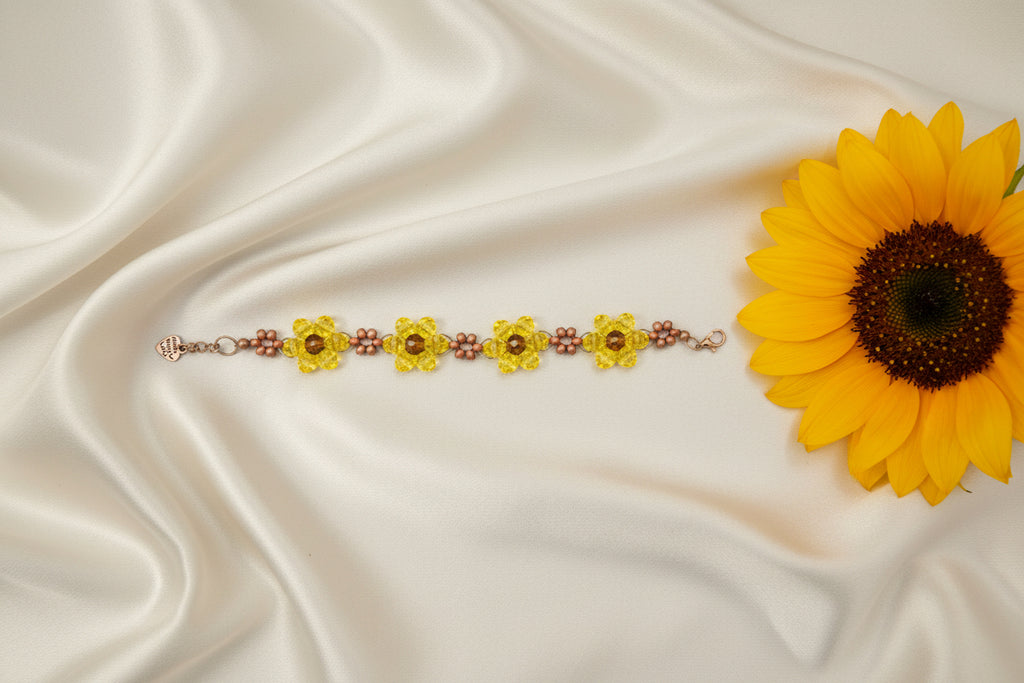 A handmade beaded bracelet featuring three yellow flower-shaped beads with brown centers, separated by rows of small brown beads, displayed on a dark textured background.