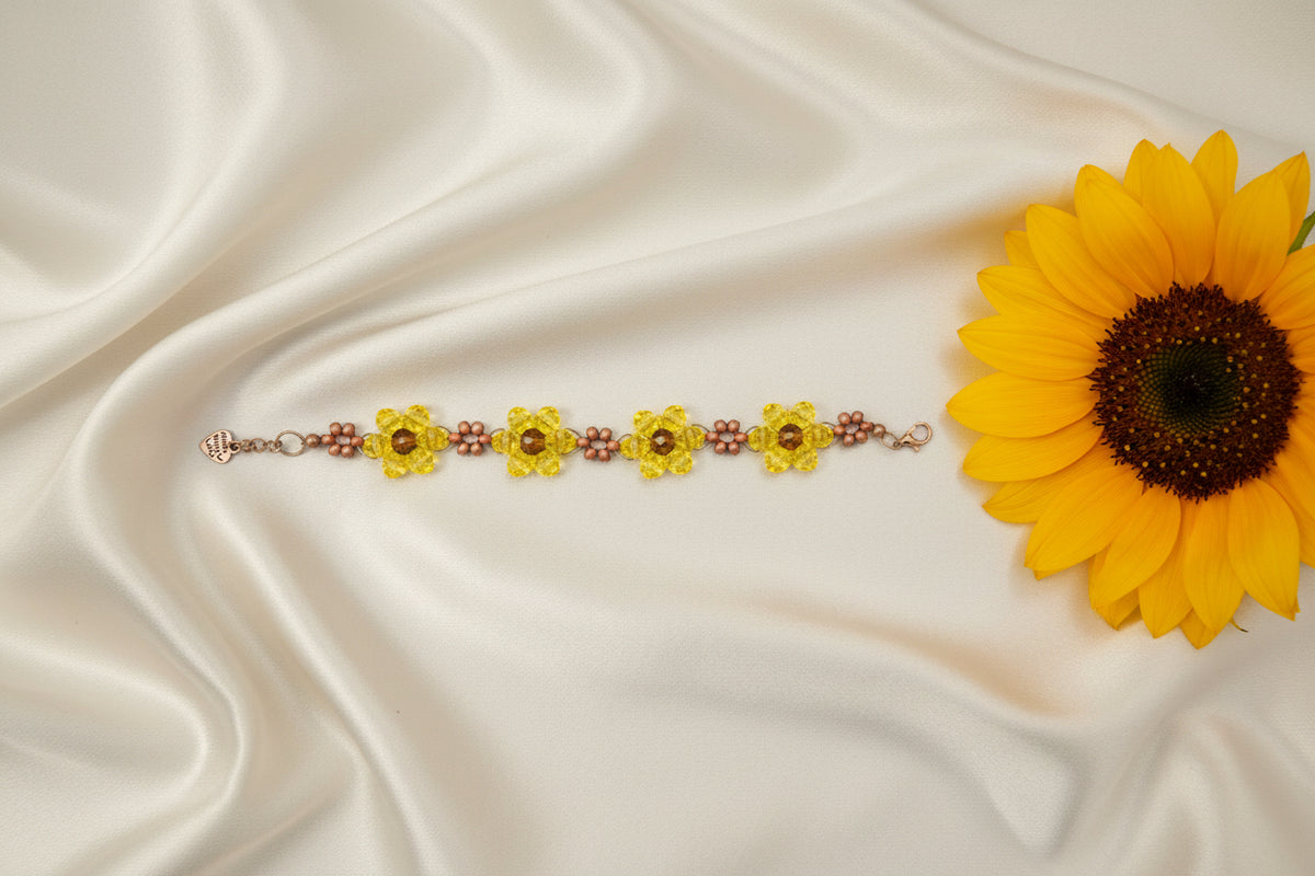 A handmade beaded bracelet featuring three yellow flower-shaped beads with brown centers, separated by rows of small brown beads, displayed on a dark textured background.