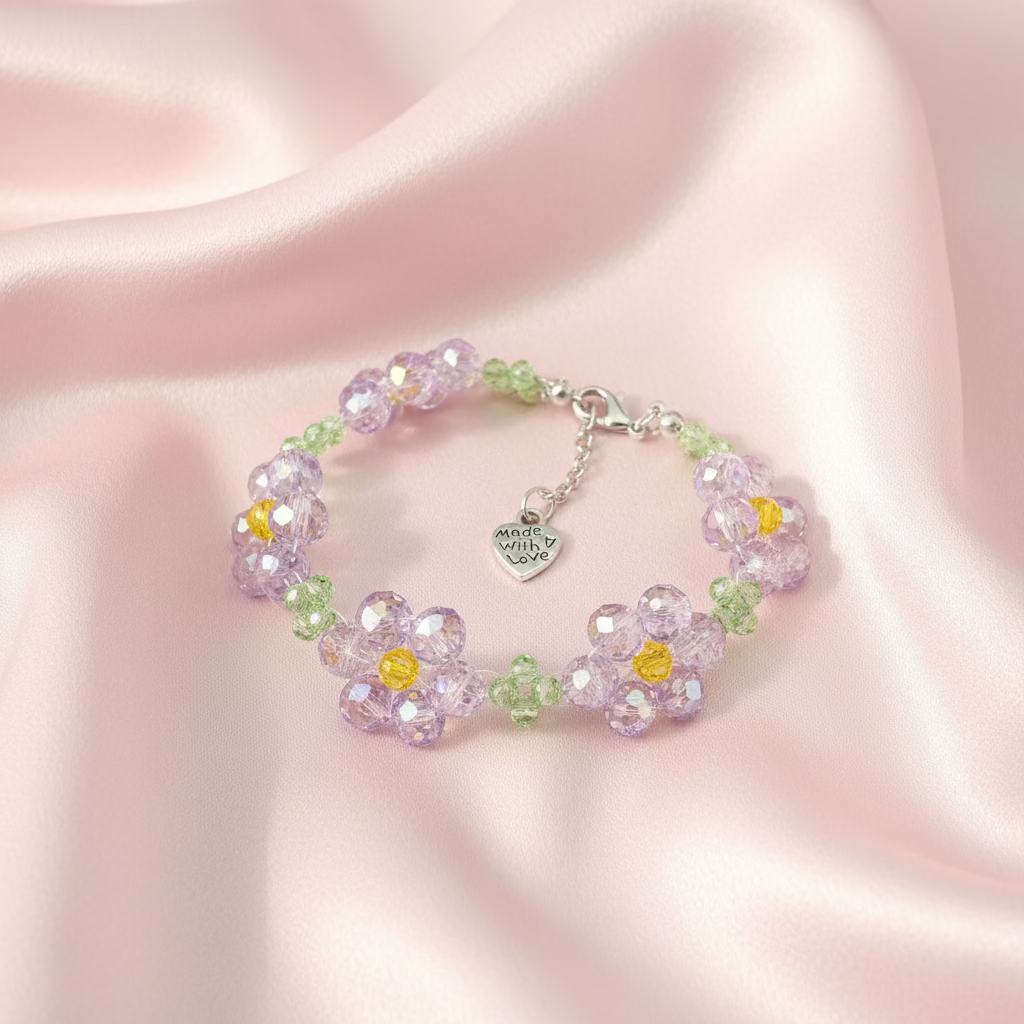 A beaded bracelet featuring faceted light purple flower-shaped beads with yellow centers, accented by small green beads and a silver heart charm, displayed on a black surface.