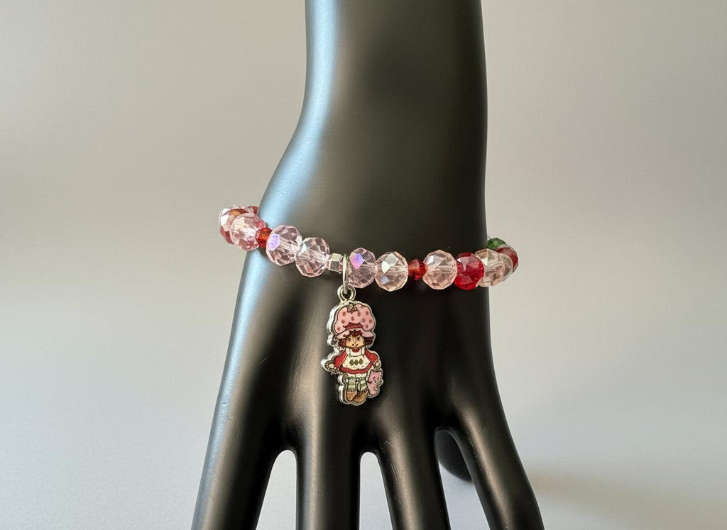 Bracelet with pink and red beads and a charm on a black mannequin hand.