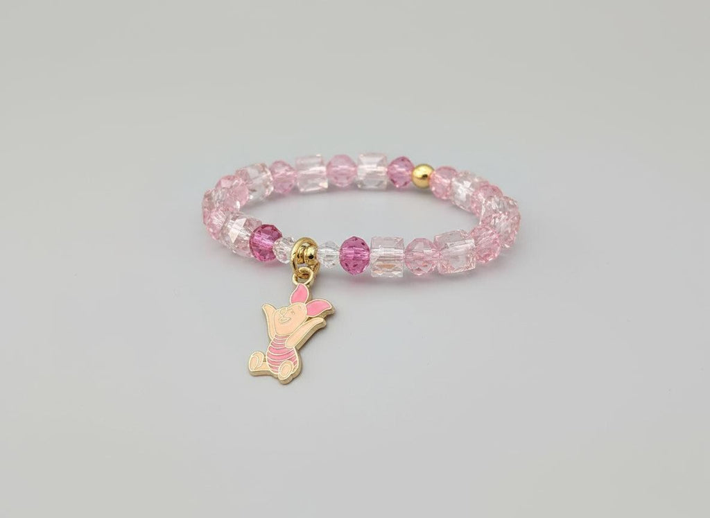 Bracelet with pink and clear beads and a gold charm on a black mannequin hand.