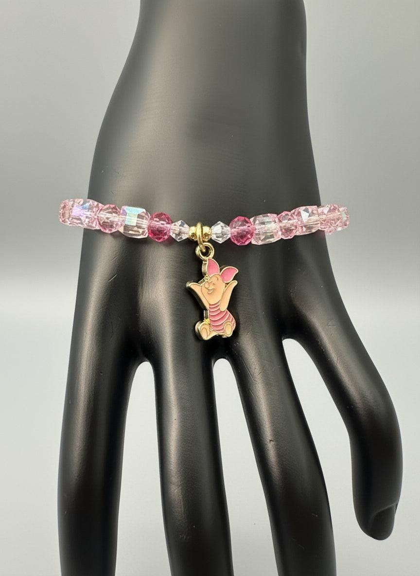 Pink beaded earring with a gold charm on a black surface