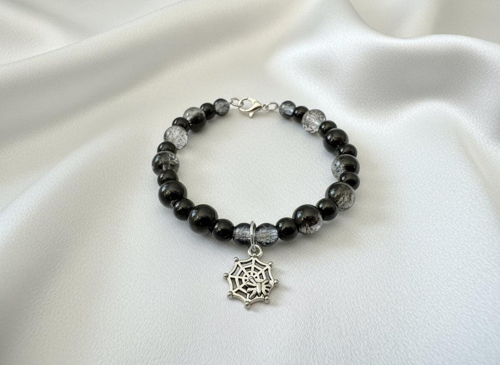 Bracelet with black beads and a spiderweb charm on a dark background