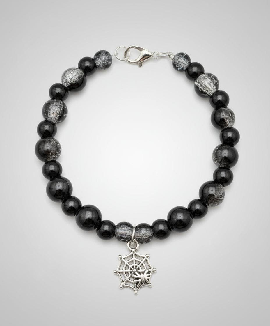 Black beaded bracelet with a silver spider web charm on a dark background