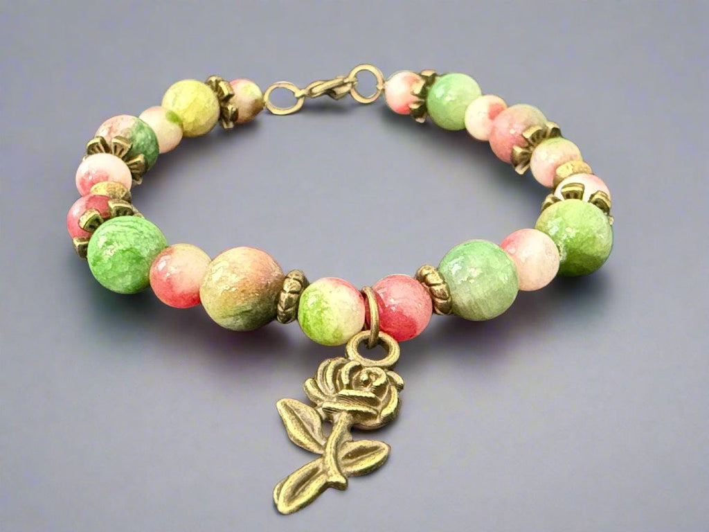 Bracelet with green and pink beads and a rose charm on a dark background