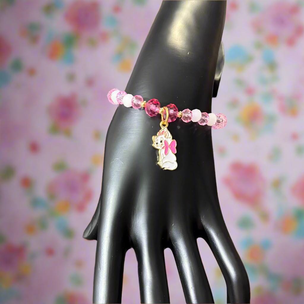 Pink beaded bracelet with a heart-shaped charm on a black mannequin hand against a dark background