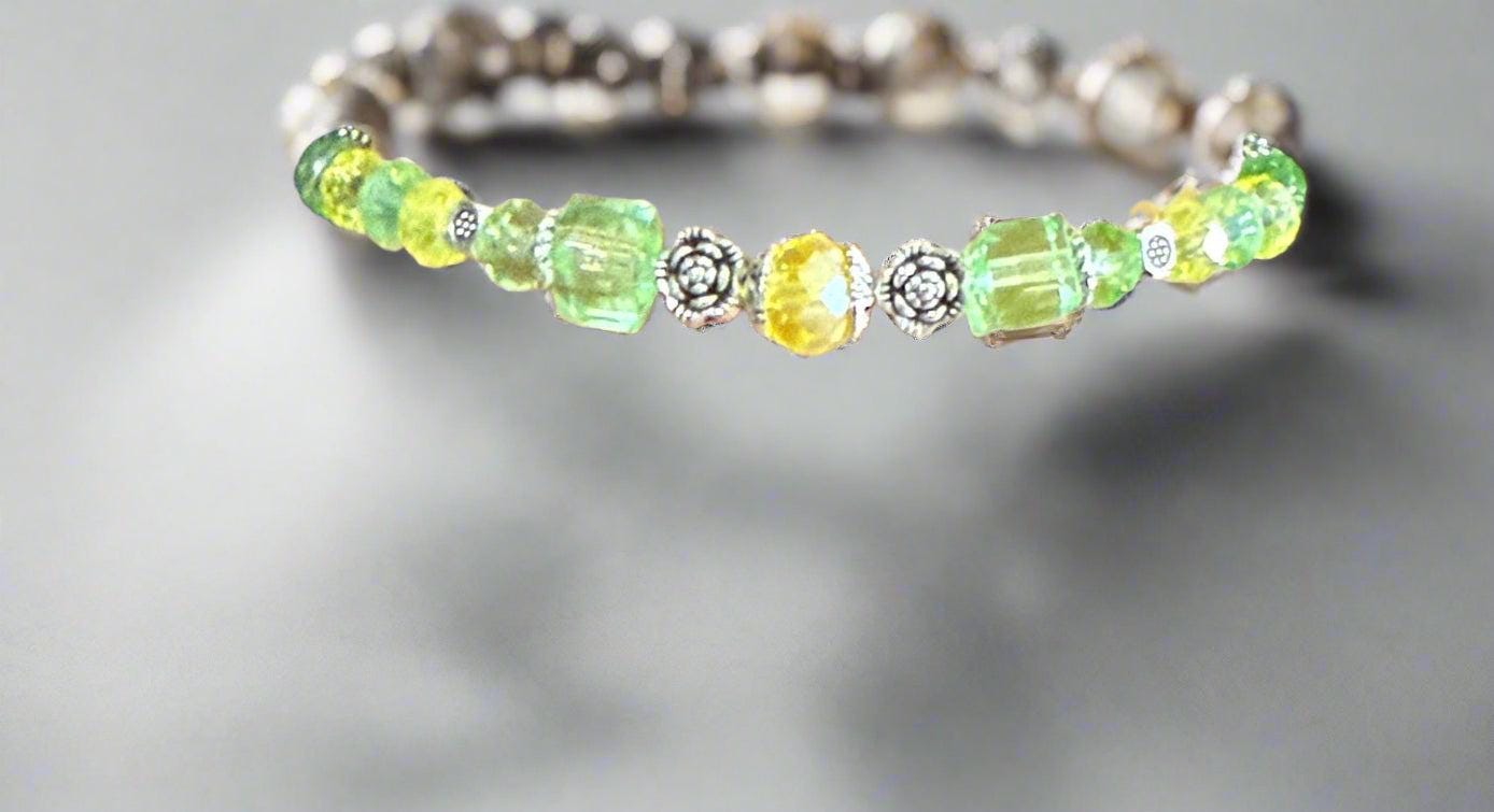 Beaded bracelet with green and yellow stones on a wrist against a black background