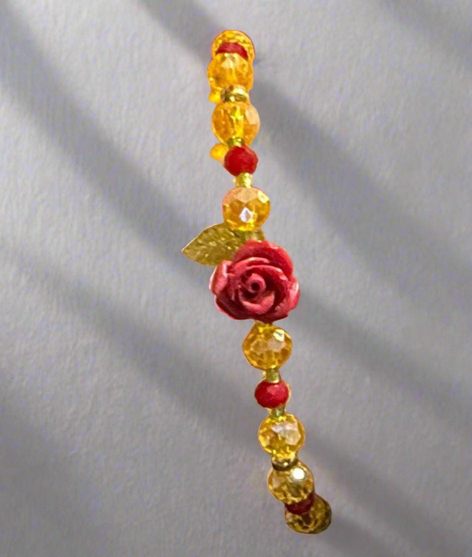 Bracelet with yellow beads and a red rose charm on a wrist.