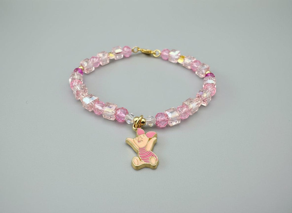 Bracelet with pink crystal beads and a gold piglet charm on a dark fabric background