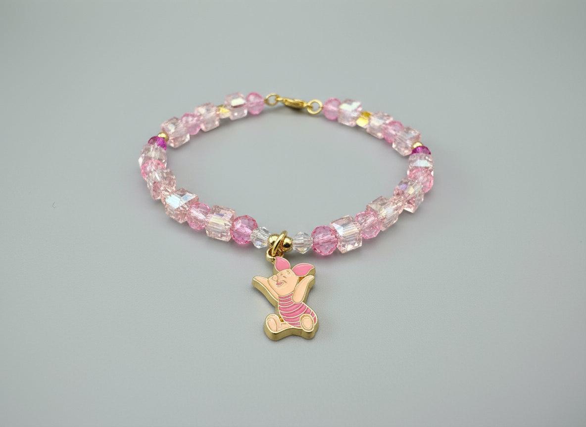 Bracelet with pink crystal beads and a gold piglet charm on a dark fabric background