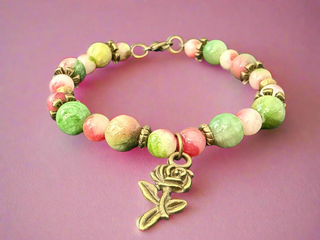 Bracelet with green and pink beads and a rose charm on a dark background
