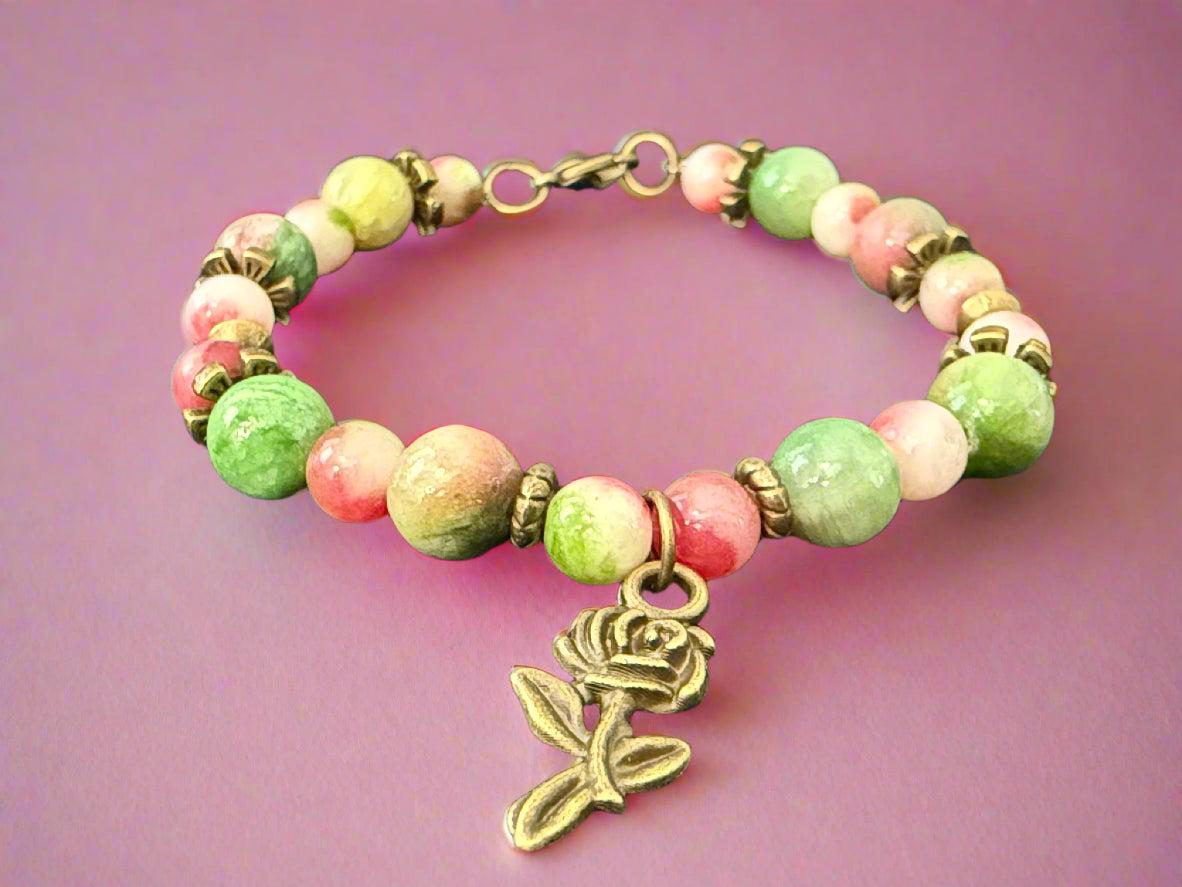 Bracelet with green and pink beads and a rose charm on a dark background