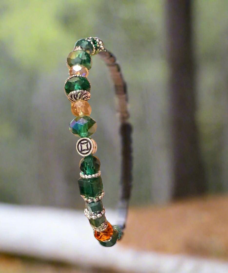 Beaded bracelet with green, orange, and silver beads on a wrist against a dark background